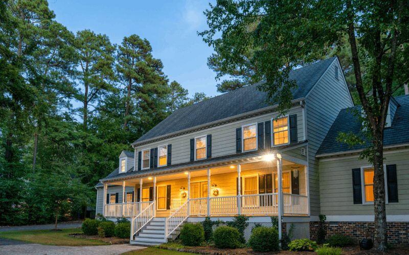 Colonial-style house with illuminated porch at dusk.